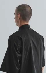 Camisa de manga corta en popelina de algodón, con diseño oversize y cierre frontal de botones. Presenta dos bolsillos delanteros, uno con solapa y otro con ojal y botón.