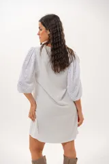 Vestido corto off-white con escote en V, de corte recto y holgado. Cuenta con mangas abullonadas tres cuartos confeccionadas en tejido broderie.