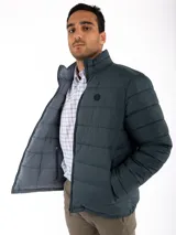 Campera puffer reversible color verde azulado con interior gris. Tiene cuello alto, cierre frontal y bolsillos laterales con cierre.