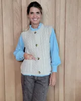 Chaleco de punto con diseño de trenzas, color beige, con cuello redondo, cierre frontal con botones y dos bolsillos delanteros.