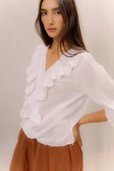 Camisa blanca de algodón con escote en V, volados delanteros con detalles de encaje y mangas largas con puños fruncidos.