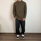 Sweater de tejido de punto grueso color verde militar, con cuello redondo y mangas largas tipo raglán. Presenta un corte holgado y una pequeña etiqueta con logo en el puño.