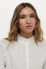 Camisa blanca de cuello mao con volados, mangas abullonadas y cierre frontal con botones.