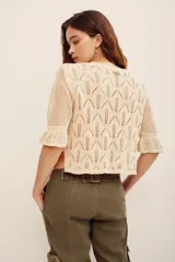 Sweater de tejido calado color beige, con escote en V y mangas cortas abullonadas. Presenta un delicado bordado floral multicolor en la parte frontal superior.