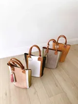 Bolso matero blanco con laterales en cuero negro con textura de cocodrilo, manijas de cuero color suela y accesorio metálico plateado en forma de cruz.