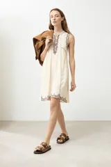 Vestido corto color crema, de corte recto y sin mangas, con bordados en el escote, sisas y ruedo.