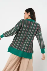 Sweater verde esmeralda de cuello redondo y manga larga, con terminación acanalada en puños y ruedo. Presenta tajos laterales y diseño de rayas verticales en tonos blanco y rosa.