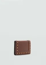 Billetera de tamaño pequeño en color marrón, con diseño de solapa y detalle de tachuelas metálicas doradas en el contorno. Cuenta con compartimento para billetes, múltiples ranuras para tarjetas y bolsillo interior con cierre.