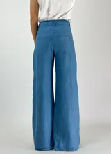 Pantalón de lino azul de corte palazzo, tiro alto y pierna ancha. Presenta costuras a la vista en color blanco y botón metálico.