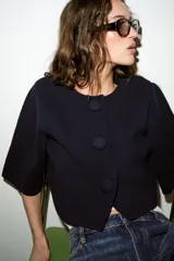 Chaqueta corta de punto color azul marino, de cuello redondo, manga por debajo del codo y cierre frontal con botones forrados al tono.