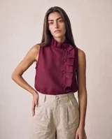Blusa sin mangas de lino color borravino, con cuello alto plisado, cartera lateral asimétrica con pliegues y botones forrados al tono.