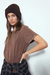 Remera de manga corta color marrón con escote a la base y calce relajado. Las mangas presentan terminación con ojales metálicos.