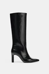 Bota de caña alta con acabado efecto acharolado, diseño de punta fina y tacón alto fino.
