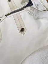 Chaqueta color beige con cierre frontal y detalles de tiras horizontales en el frente y hombros con botones metálicos.