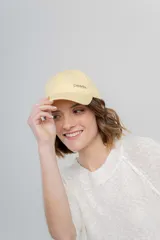 Gorra verde militar de diseño clásico con visera curva y aplique metálico plateado con la inscripción "Peach" en el lateral frontal. Cuenta con tira ajustable en la parte trasera.