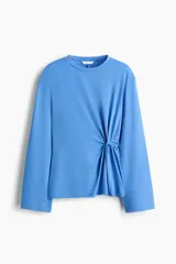 Top de punto color celeste, de manga larga amplia, con hombros caídos, escote redondo y detalle de nudo o giro drapeado en la cintura.