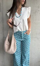 Musculosa blanca de diseño ligero con escote en V y sutiles detalles bordados tonales en el frente, complementada con volados en las sisas.