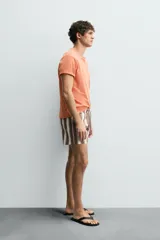 Bañador de hombre con estampado de rayas verticales anchas en tonos marrón oscuro y beige claro, con finas líneas rosadas entre ellas. Posee cintura elástica con cordón ajustable y forro interior.