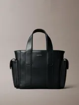 Cartera tote estructurada Calvin Klein de piel sintética lisa en color negro, con asas superiores de mano, compartimentos exteriores en los laterales y logo metálico grabado en la parte delantera.
