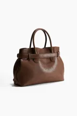 Bolso tote marrón con doble asa corta, cierre superior con cordón ajustable y cinturón decorativo con hebilla metálica dorada.