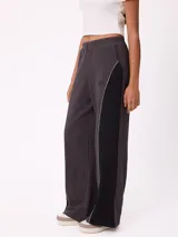 Pantalón tipo babucha de corte holgado y tiro alto, confeccionado en una combinación de gris oscuro y negro con una línea divisoria clara. Cuenta con cintura elástica y un pequeño logo circular bordado en la parte superior.