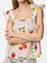 Top corto sin mangas con cuello cuadrado y tirantes ajustables con lazo. Presenta un estampado de frutas (fresas, limones/naranjas) y un patrón de cuadros en tonos verde, amarillo y rosa pálido. El borde del escote y el ruedo tienen un ribete ondulado verde.