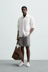 Bermuda negra de corte recto, con cintura elástica ajustable mediante cordón, pliegues frontales y bolsillos de vivo en la espalda. El bajo tiene un dobladillo vuelto.