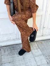 Sueco de plataforma color negro, confeccionado en material sintético tipo gamuza. Presenta una tira frontal con hebilla metálica y ojales decorativos, con suela dentada de goma.