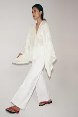 Blusa tipo capa de algodón con escote en pico y mangas largas amplias. Presenta bordados florales a tono en toda la prenda, bajo asimétrico y cierre frontal con botones.