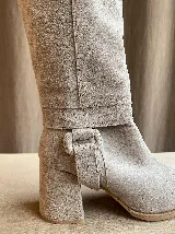 Botas de caña alta desmontables que se transforman en botinetas, confeccionadas en gamuza color beige. Presentan un diseño de punta semicuaadrada, taco cuadrado de 6 cm y detalle de estribo con hebilla forrada en el tobillo.