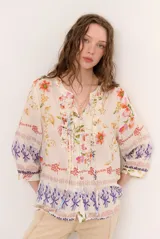 Blusa de manga tres cuartos color beige con estampado floral multicolor, escote en V y detalles de volados frontales junto a la botonadura.
