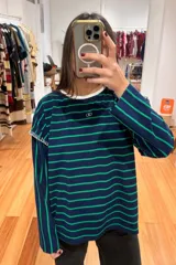 Remera de manga larga con diseño a rayas horizontales en azul marino y verde. Presenta un cuello redondo en color blanco, costuras decorativas a contratono en los hombros y un pequeño logo bordado en el centro del pecho.