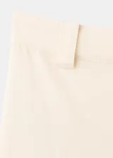 Pantalón de tiro alto color crudo, con diseño largo y corte recto. Cuenta con trabillas, bolsillos laterales y cierre frontal oculto con cremallera, botón y ganchos.