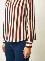 Blusa de color blanco con cuello en V y mangas largas con puños abotonados. Presenta un diseño de corte recto y holgado.