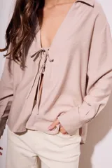 Blusa color visón con escote en V profundo y lazos ajustables en el frente, mangas largas y corte holgado.