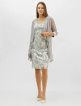 Conjunto de dos piezas compuesto por un vestido midi de silueta recta con tejido plisado metalizado y escote redondo con pedrería, acompañado por una chaqueta de gasa abierta con caída en cascada y mangas tres cuartos con puños metalizados.