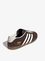 Championes Adidas Gazelle Lo Pro, modelo de corte bajo confeccionado en gamuza marrón con las tres tiras características en blanco, cordones blancos y suela de goma translúcida.