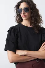 Remera negra de algodón con cuello redondo y mangas cortas con volados en capas que aportan volumen y movimiento.