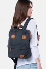 Mochila de lona gris oscuro con detalles en cuero sintético marrón, asas superiores y bolsillo frontal con cierre.