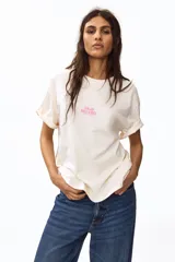 Remera oversized en punto de algodón color beige, de cuello redondo y manga corta, con estampa frontal pequeña en tono rosado con la inscripción "Solar Treasures".