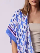 Kimono tejido con estampado abstracto en tonos azules, blancos y violetas. Tiene terminación de ruedo con borlas.