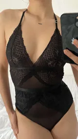 Body de encaje y microtul negro con diseño de escote halter, espalda descubierta y cierre con ganchos. Presenta paneles de encaje floral y secciones de tul transparente.