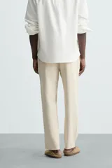 Pantalón de corte relajado color beige confeccionado en tejido de mezcla de algodón y lino. Posee cintura elástica ajustable con cordón, bolsillos frontales y bolsillos traseros de vivo.