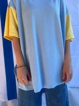 Remera de corte oversize confeccionada en tejido de punto acanalado color celeste, con mangas cortas en color amarillo y detalle de parche bordado con la bandera de Uruguay en la parte superior de la espalda.