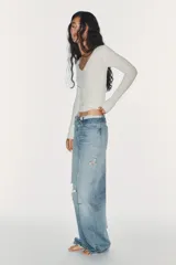 Jeans de mezclilla de tiro medio, corte wide leg y diseño relaxed. Presenta detalles rotos y desgastados en las piernas, y una cinturilla doblada superpuesta con trabillas y cierre frontal con cremallera y botón metálico.