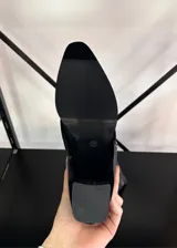 Botas altas de mujer color negro, estilo cowboy, con caña ancha y puntera afilada. Presentan un acabado liso y un tacón bajo y ancho.