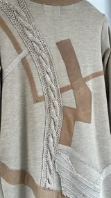 Sacon de lana color beige con diseño de paneles asimétricos, detalles en cintas de cuero y aplicaciones de tejido de punto grueso con trenzado. Presenta corte recto y largo midi.