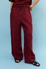Pantalon ancho de lino color bordó con costuras decorativas en zigzag de color rojo y cordón ajustable en la cintura con cuentas en los extremos.