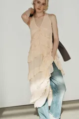 Vestido midi de escote en pico con lazada frontal y diseño sin mangas. Presenta múltiples niveles de volantes a lo largo de la falda y cierre lateral con cremallera oculta.