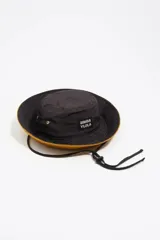 Gorro tipo bucket Bimba y Lola de color negro, con interior en color mostaza y cordón ajustable con tanca. Presenta etiqueta con el logo de la marca en el frente y ojales metálicos laterales.